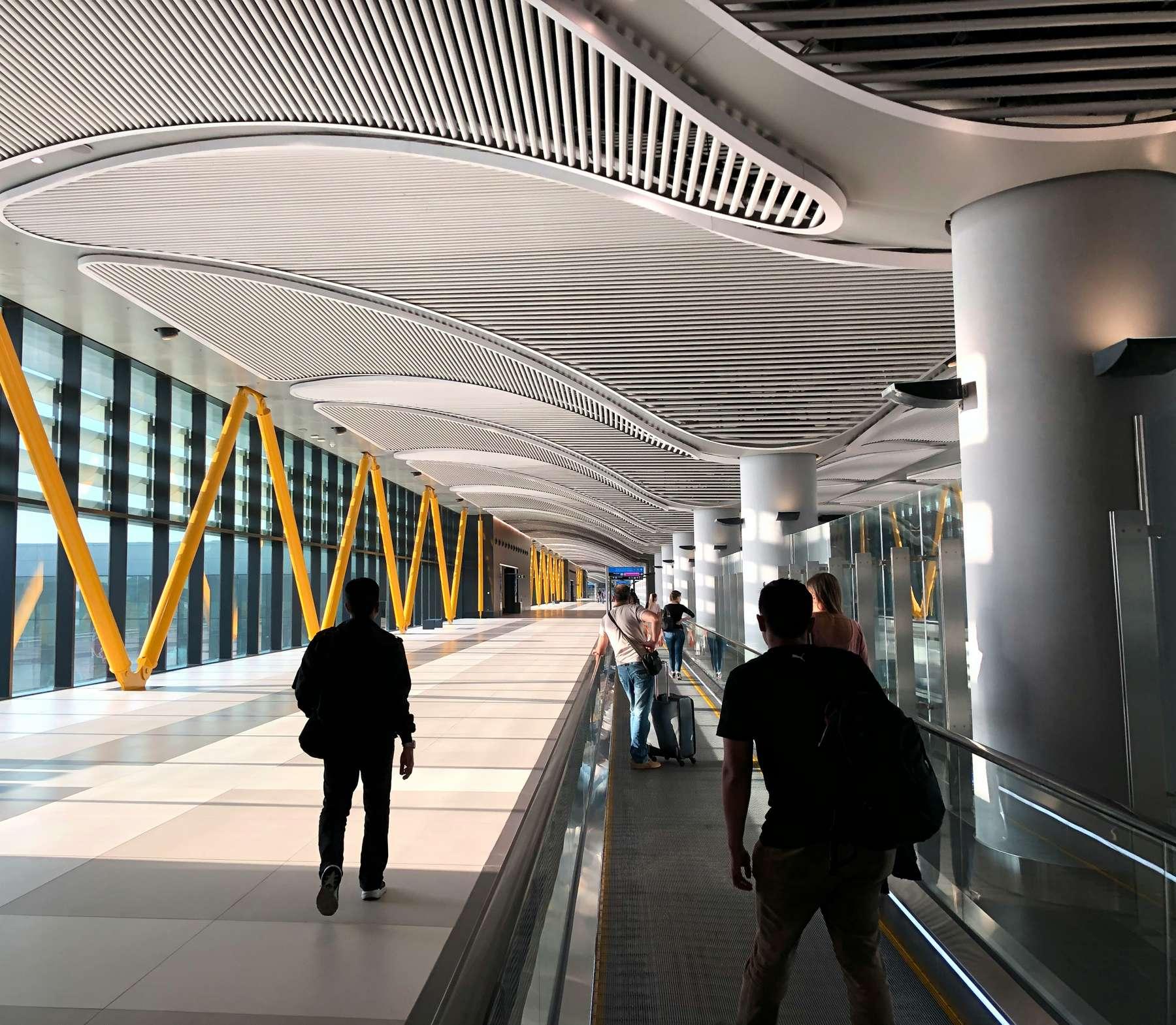 Passengers on a moving walkway beneath a curved white ceiling, Istanbul Airport
