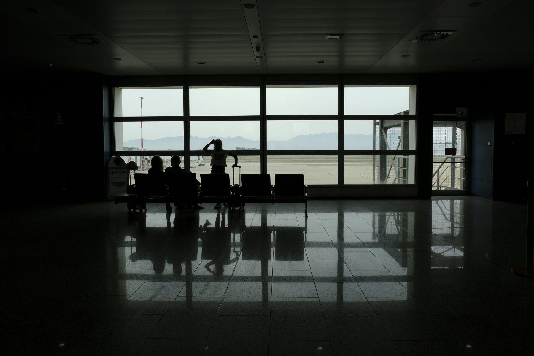 Silhouetted passengers at a gate window looking out at the apron